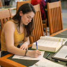 girl sitting in Shields Library writing on a notebook