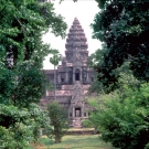 A temple of Angkor Wat shown behind arching trees and foliage on both sides.