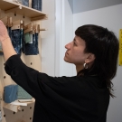 A person inspects a fabric sample hanging off a wooden peg on a craft board mounted on the wall.