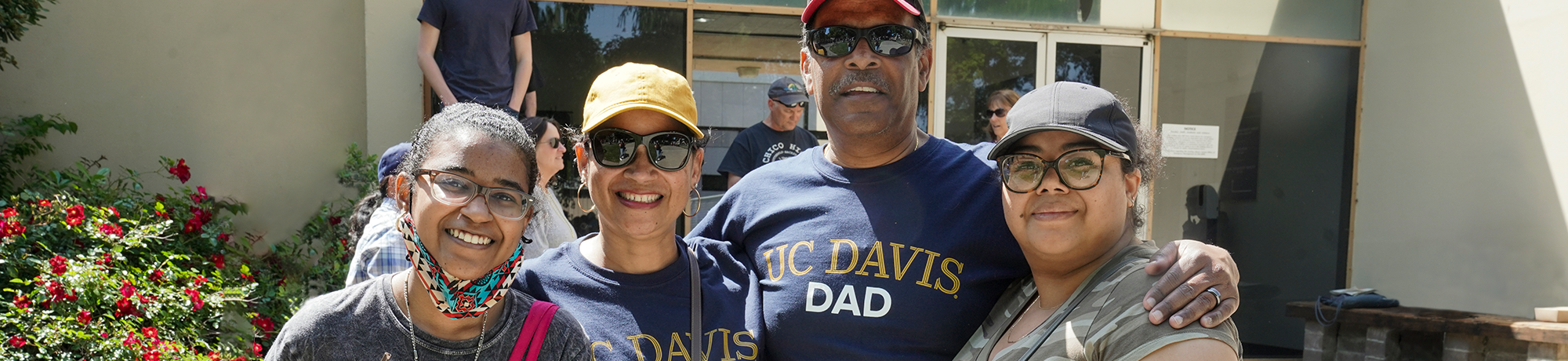 UC Davis family posing, mom, dad, and two daughters, posing for a picture together. Mom's shirt says "UC Davis Mom" and dad's shirt days "UC Davis Dad".