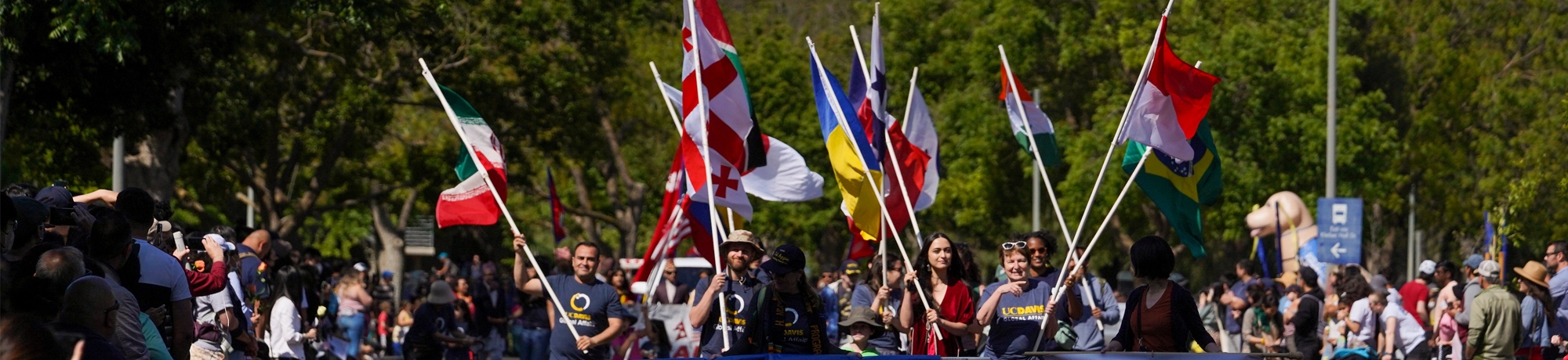 Group of Global Affairs staff and community members holding various countries' flags while marching in a parade.