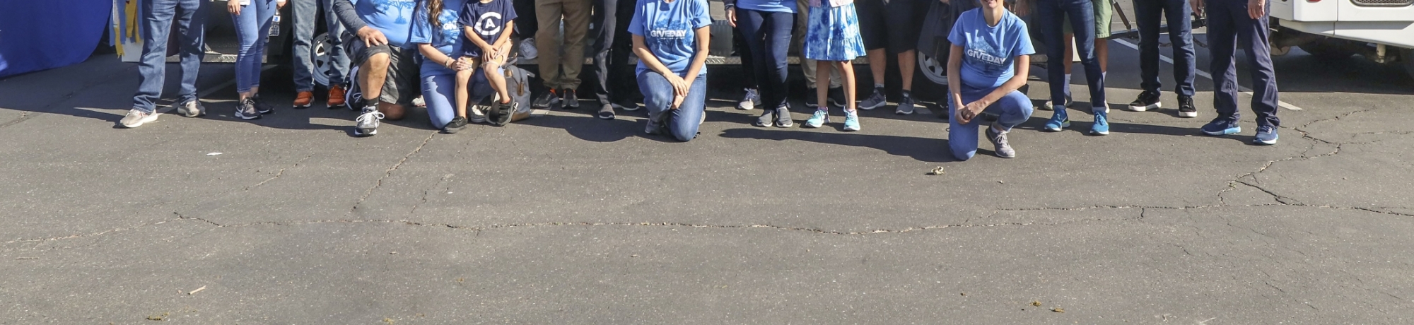 A group of volunteers wearing matching blue &#34;Give Day&#34; shirts pose for a photo in front of the tram as part of the Picnic Day parade.