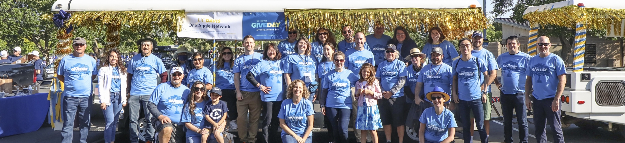 A group of volunteers wearing matching blue &#34;Give Day&#34; shirts pose for a photo in front of the tram as part of the Picnic Day parade.