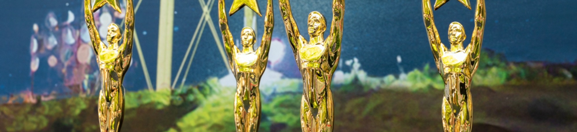 A row of four gold statue trophy awards sitting on a black sparkly sequin tablecloth draped over a cocktail table.