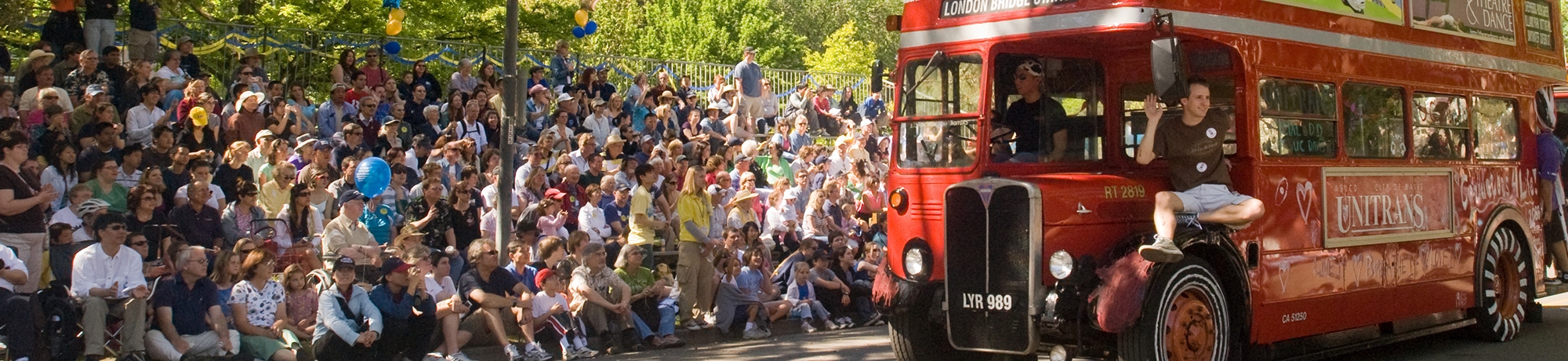 A large crowd of people at a Picnic Day parade. A vintage red double-decker Unitrans passes by.